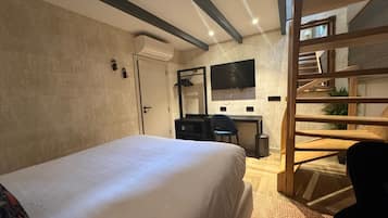 Quarto de hotel com cama, escrivaninha, cadeira, televisão e escada.