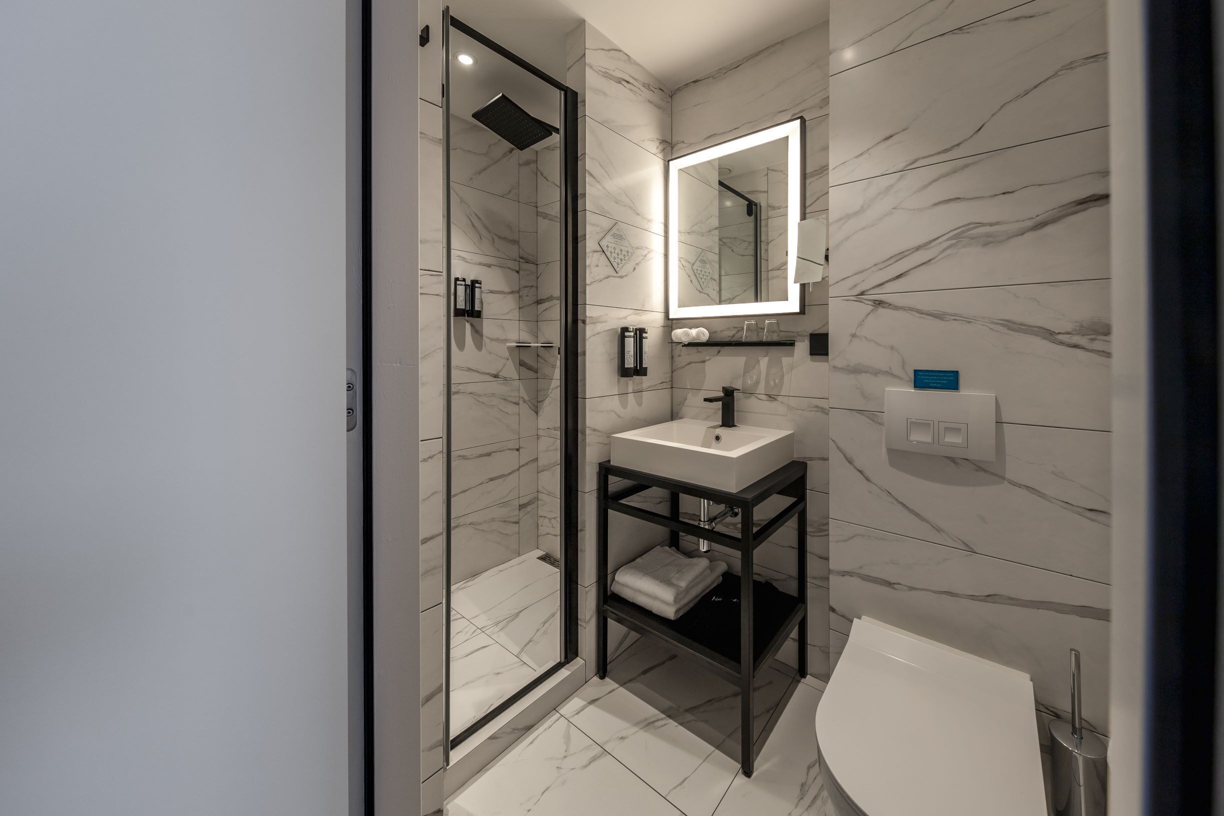 Een moderne badkamer met een douchecabine van glas, een wastafel op voet en een grote spiegel.