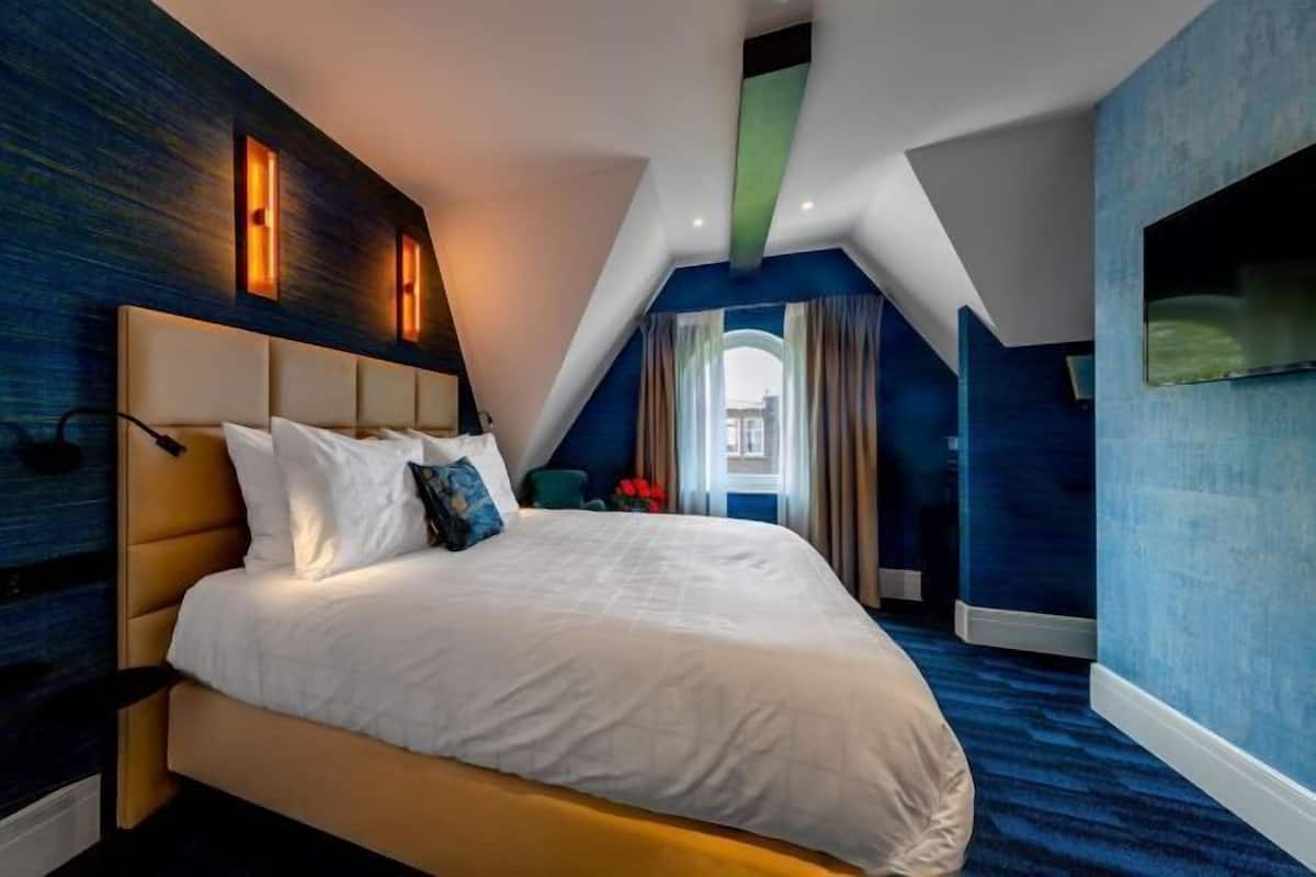 Een slaapkamer met een groot bed, een schuine balkenlaag en uitzicht op de omgeving.