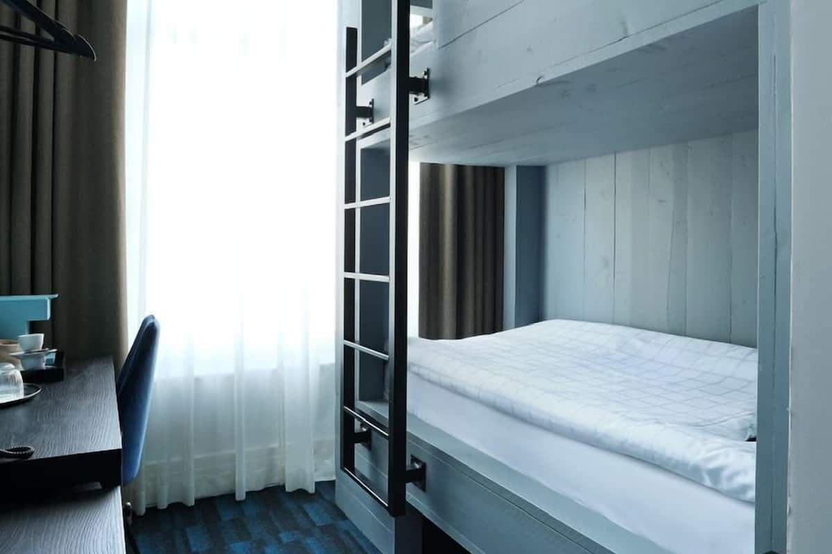 Een slaapkamer met een stapelbed, bureau, stoel en een klein tafeltje.