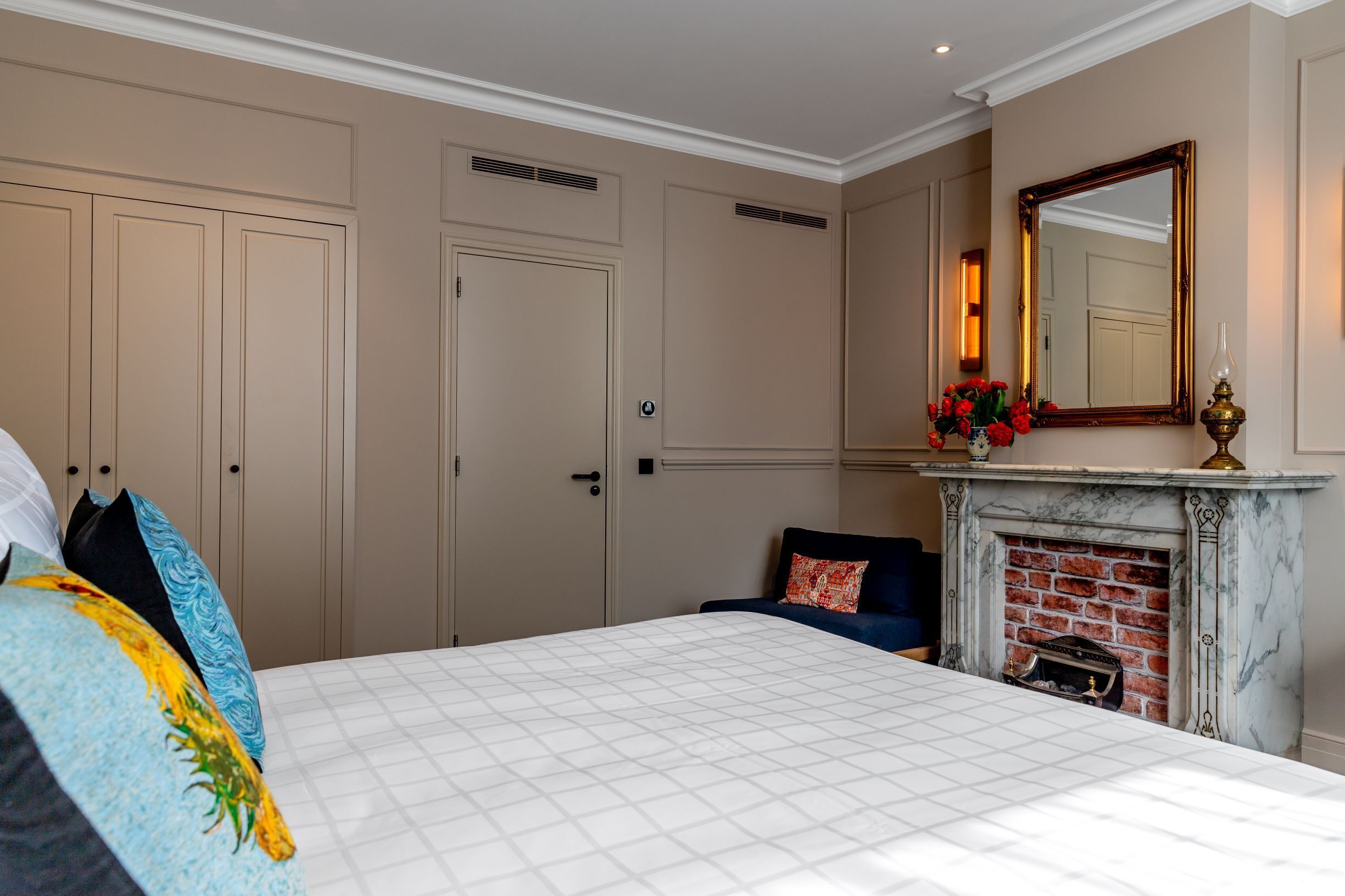A bedroom with a large bed, a fireplace, a mirror, and a wardrobe.