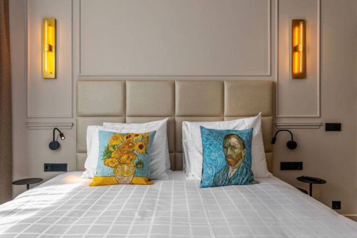 A hotel room with a large bed, two wall-mounted light fixtures, and a nightstand with a lamp.