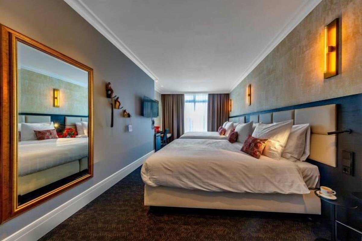 Een hotelkamer met een groot bed, een spiegel, een televisie en uitzicht op de stad.