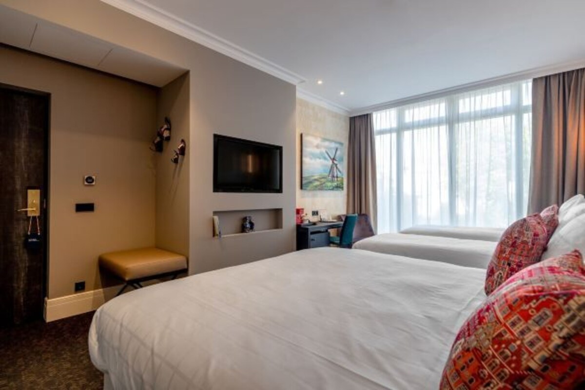 A hotel room with two beds, a desk, a TV, and a painting on the wall.