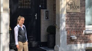 Een vrouw staat bij de ingang van een gebouw met een zwarte deur en een bord waarop staat: De Ware Jacob Boutique Hotel.