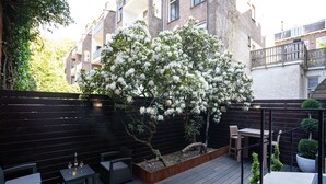 Een terras met buitenmeubilair, een kleine tafel met glazen en een potplant.