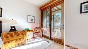 Una habitación con escritorio de madera, una silla, una lámpara y un ventanal corredera que da a un espacio exterior.