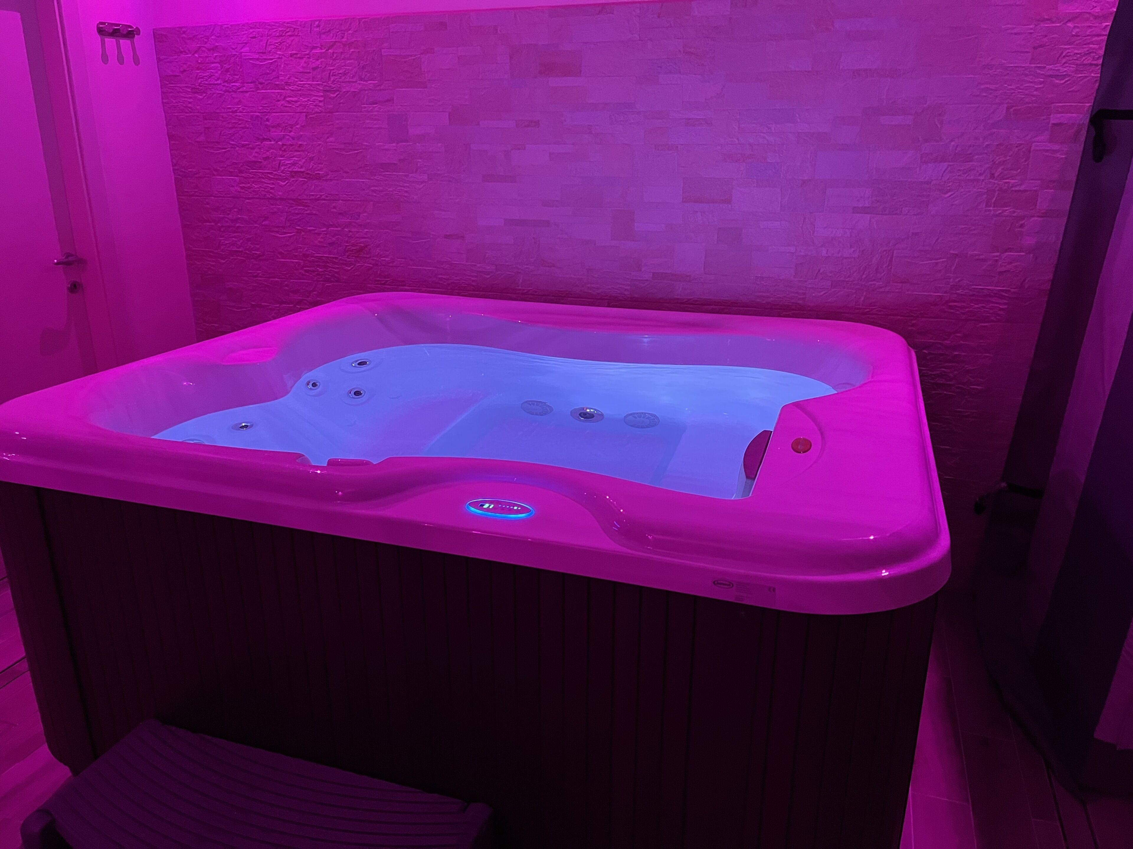 A hot tub with a control panel, set against a textured wall.