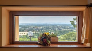 Una ventana con vistas al paisaje, una lámpara y un florero con flores.