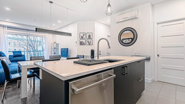 A modern kitchen with a central island, a built-in dishwasher, and a large window offering a view of the cityscape. - The Kaméléon, The hut (Québec City)
