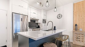 A modern kitchen with a central island, stainless steel appliances, and a wooden accent wall. - The Kaméléon, The hut (Québec City)