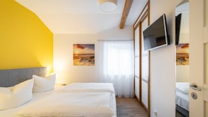 Habitación de hotel con dos camas, un televisor montado en la pared y un ventanal con cortinas translúcidas.