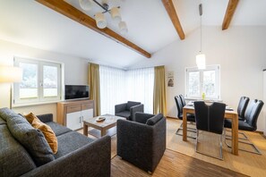 A modern living room with a sofa, armchairs, a TV, and a dining area with chairs and a table.