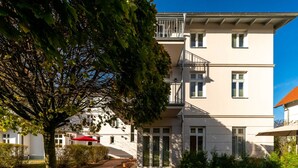 A multi-story building with a garden area, a tree, and a red umbrella. - Vacation apartment Brise at Ostsee-Domizil Sandburg - Holiday apartment Brise (Kühlungsborn (Ostseebad))