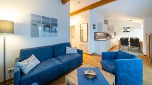 A modern living room with a blue sofa, a coffee table, and a dining area with chairs. - Vacation apartment Brise at Ostsee-Domizil Sandburg - Holiday apartment Brise (Kühlungsborn (Ostseebad))