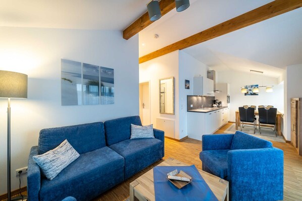 A modern living room with a blue sofa, a coffee table, and a dining area with chairs.