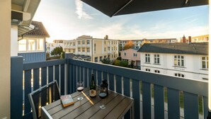 A balcony with a wooden table, two wine glasses, and a bottle of wine. - Vacation apartment Brise at Ostsee-Domizil Sandburg - Holiday apartment Brise (Kühlungsborn (Ostseebad))