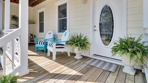 Een houten terras met twee blauwe stoelen en een potplant nabij een witte deur met een ovaal raam.