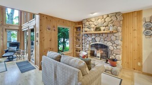 Una sala de estar acogedora con chimenea de piedra, paredes de madera y un espacio de descanso cómodo con sofá y sillones.