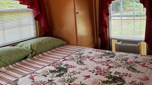 Un dormitorio con techo de madera, una cama con colcha floral, cortinas rojas y una ventana con persianas.