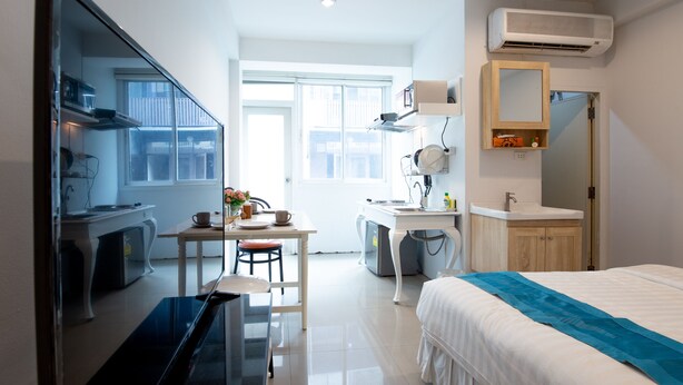 Ein kleines Hotelzimmer mit Bett, Schreibtisch, Stuhl, einer kleinen Küchenzeile und einem Badezimmer.