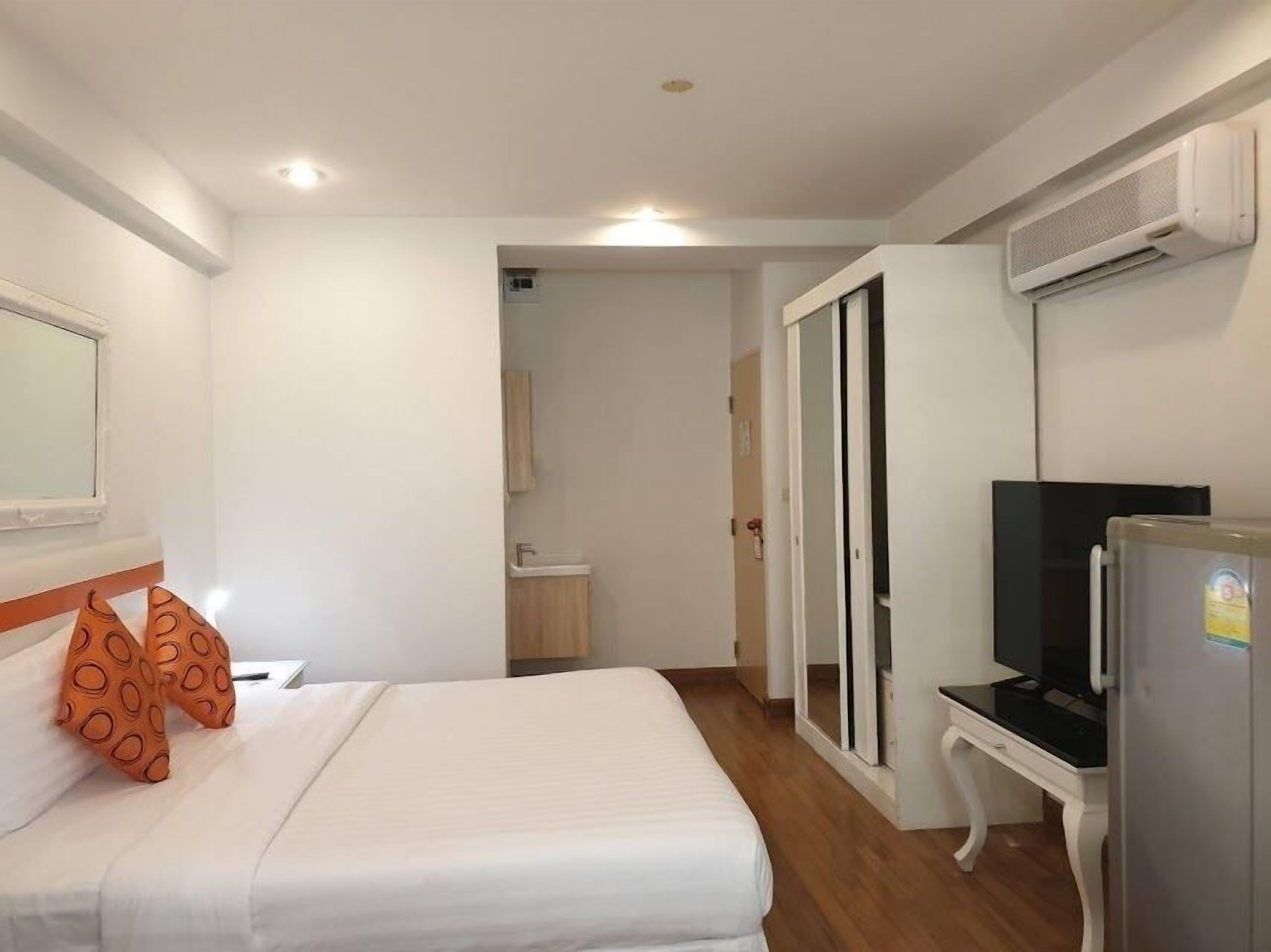 A hotel room with a bed, a TV, a desk, and an air conditioning unit.