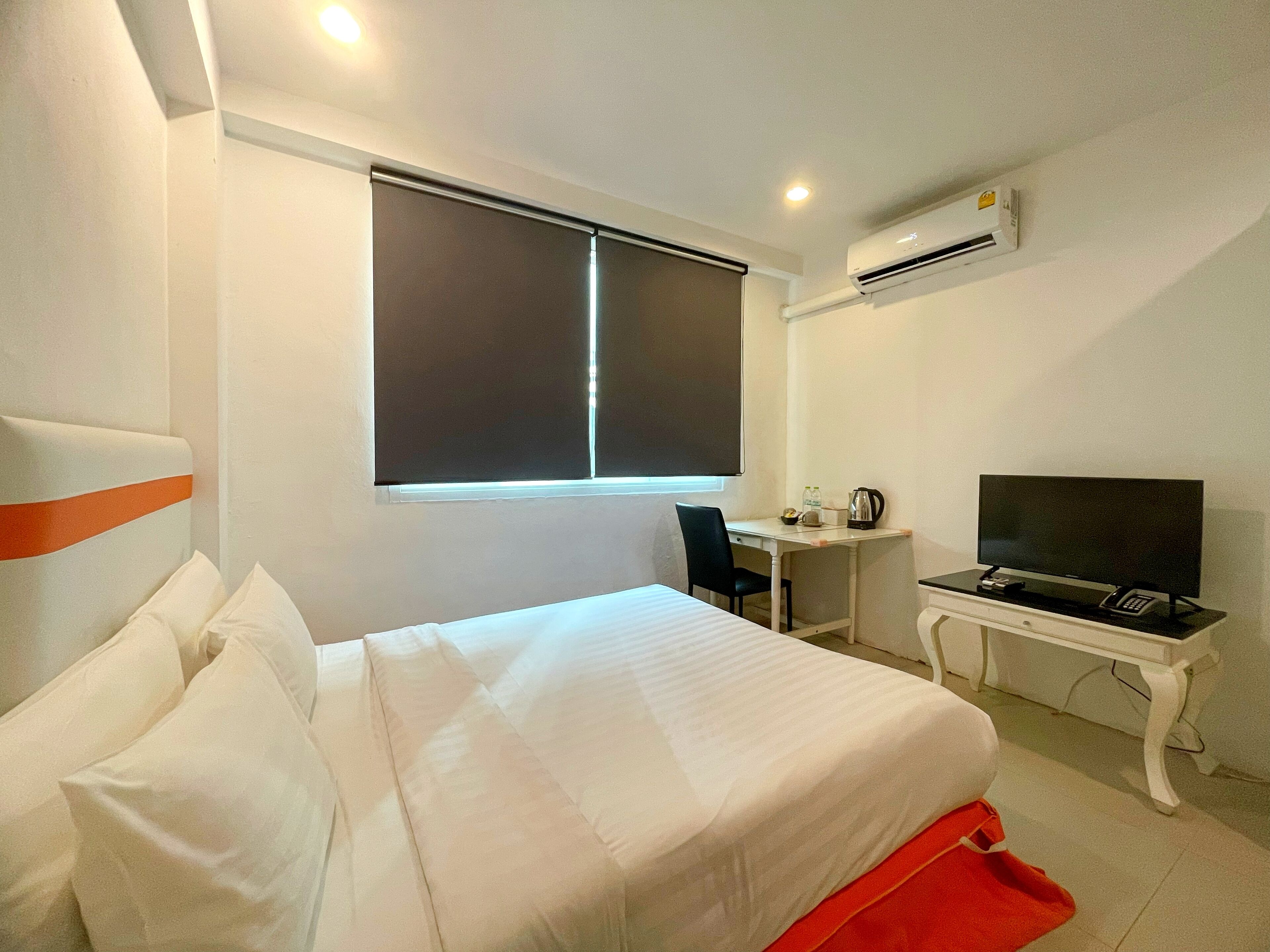 A hotel room with a bed, a desk, a television, and an air conditioning unit.
