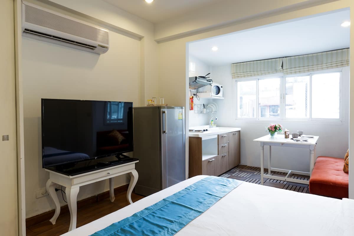 Una habitación de hotel con cama, televisor, kitchenette, una mesita y ventana.