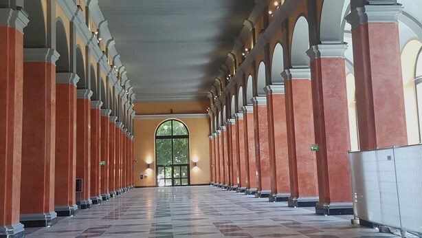 Un largo pasillo con piso estampado, columnas en arco y una puerta central.