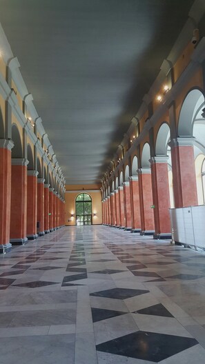 Un lungo corridoio con pavimento decorato, colonne ad arco e una porta centrale.