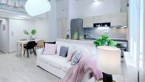 Una sala de estar moderna con un sofá blanco, una mesa de comedor y una cocina al fondo.