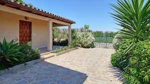 A stone-paved courtyard with a covered entrance, a wooden door, and surrounding greenery. - MAGDALENA, traditional villa near the town. (Pollensa)