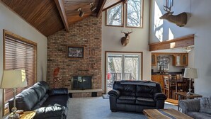 A spacious living room with a stone fireplace, leather sofas, and a dining area with wooden furniture. - Escape to Serenity at The Covered Bridge Hideaway-The Perfect Vacation Rental!
 (Fennimore)