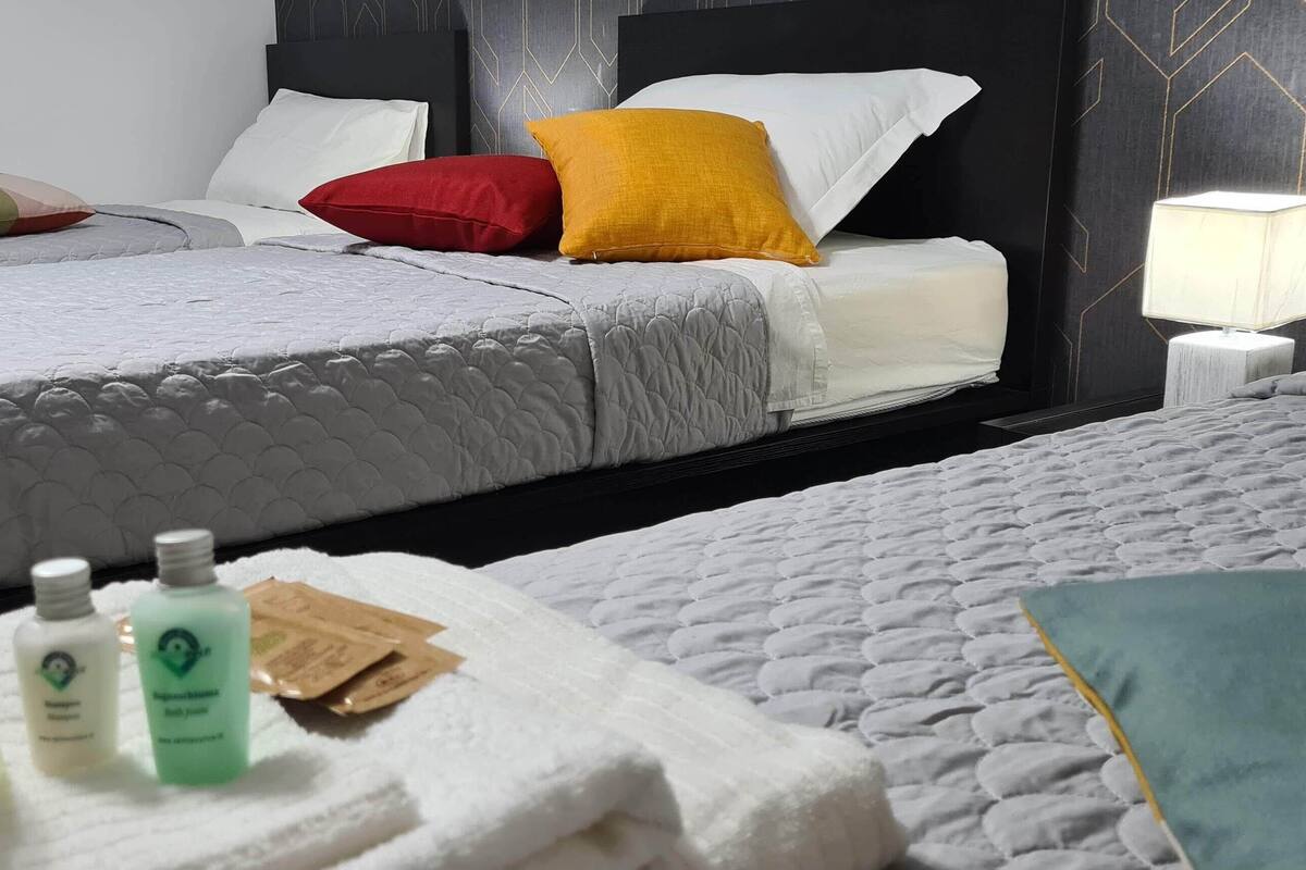 Ein Hotelzimmer mit zwei Betten, einem Nachttisch und einer Beistelltisch mit Lampe. Auf den Betten liegen Toilettenartikel und am Boden ein Handtuch.