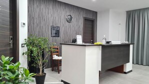 A modern reception area with a reception desk, a clock, a small plant, and a chair. - Idilliaco Inn (Motta Sant'Anastasia)
