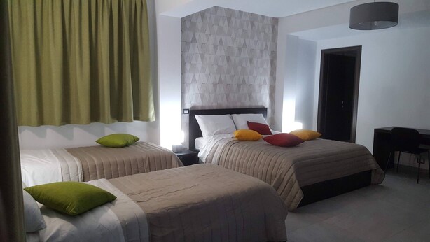 A hotel room with two beds, each with a different color pillow, a desk, and a chair. - Idilliaco Inn (Motta Sant'Anastasia)