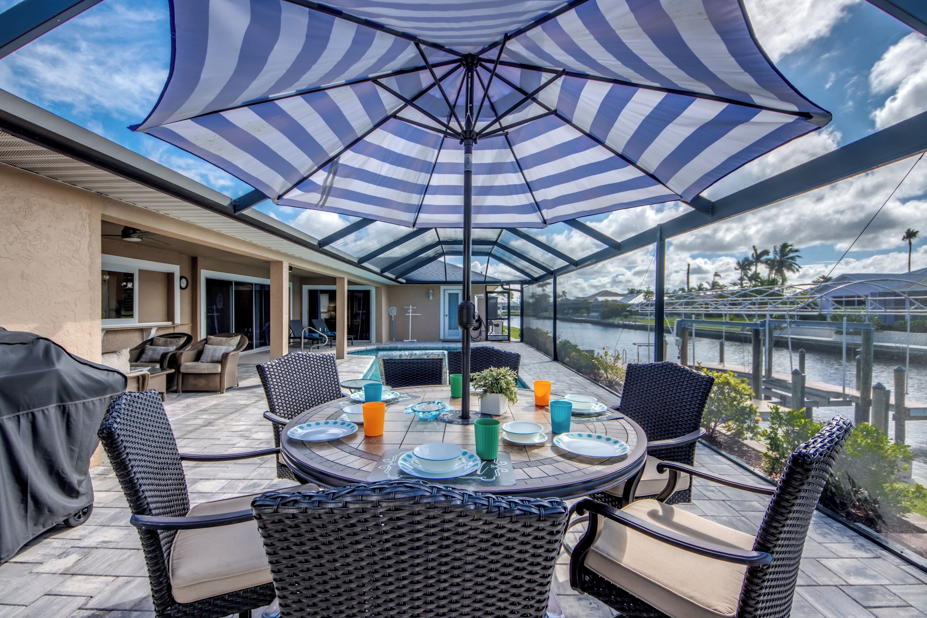 Un patio exterior con mesa y sillas cubiertas, con vistas a una masa de agua.