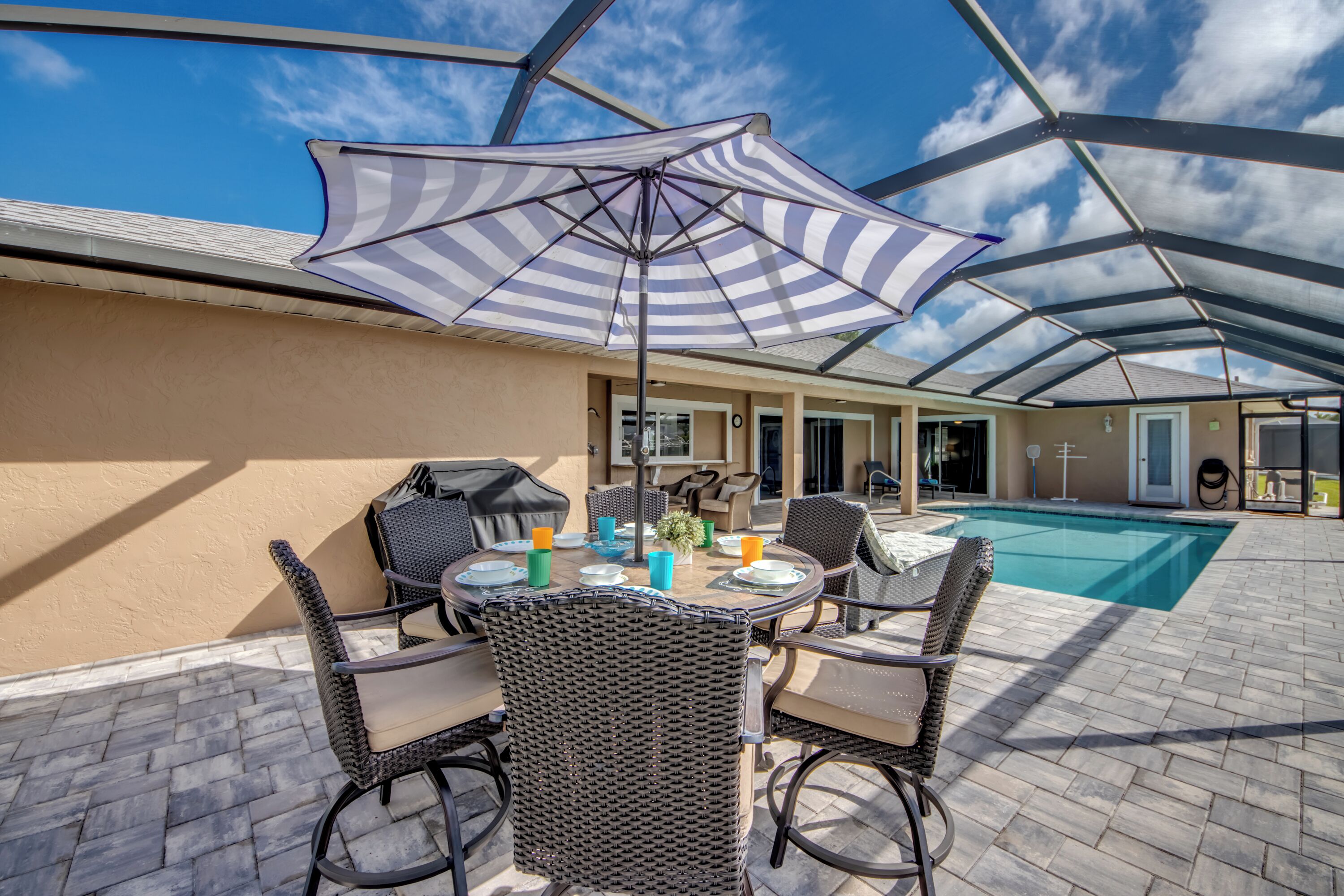 En udendørs terrasse med swimmingpool, fletmøbler og en stribet parasol.