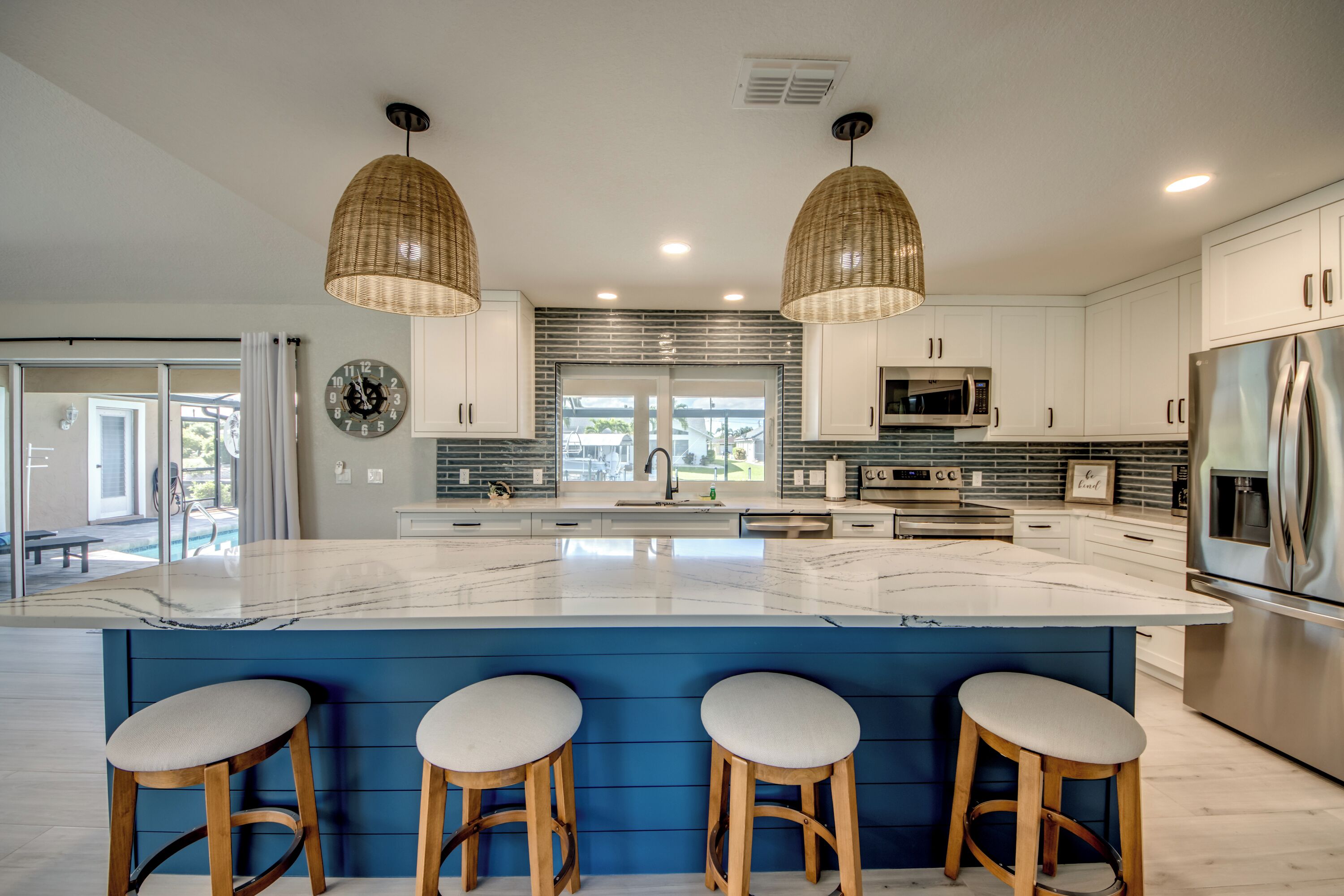 A modern kitchen with a large island, white cabinets, stainless steel appliances, and wicker pendant lights.