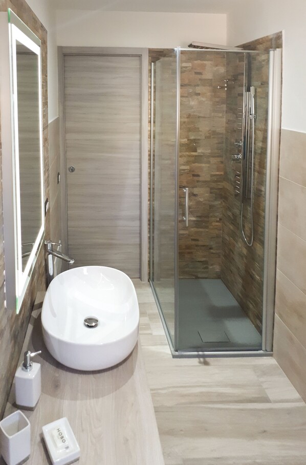 Ein modernes Badezimmer mit einem runden Waschbecken, einer Glasdusche und einem Holzlagerplatz.