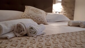 Un lit avec des serviettes enroulées, une couvre-lit à motifs et un mur de pierre en arrière-plan.