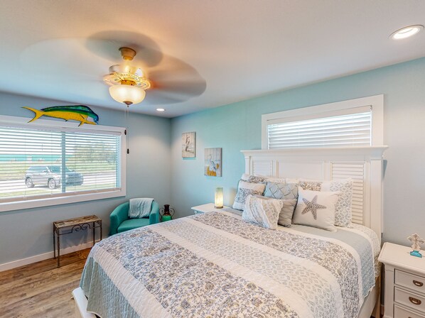 Une chambre à coucher comprenant un lit, une table de chevet, une chaise, une fenêtre avec des stores et un ventilateur de plafond.