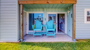Ein zweistöckiges Haus mit einer überdachten Veranda, zwei türkisfarbenen Adirondack-Stühlen und einem kleinen Tisch.