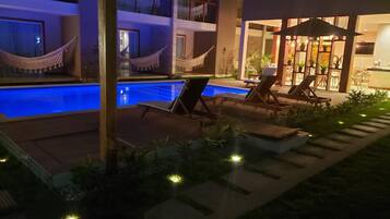 Un área de piscina con sillones reclinables y hamacas, rodeada por un edificio de varios pisos y grandes ventanales.