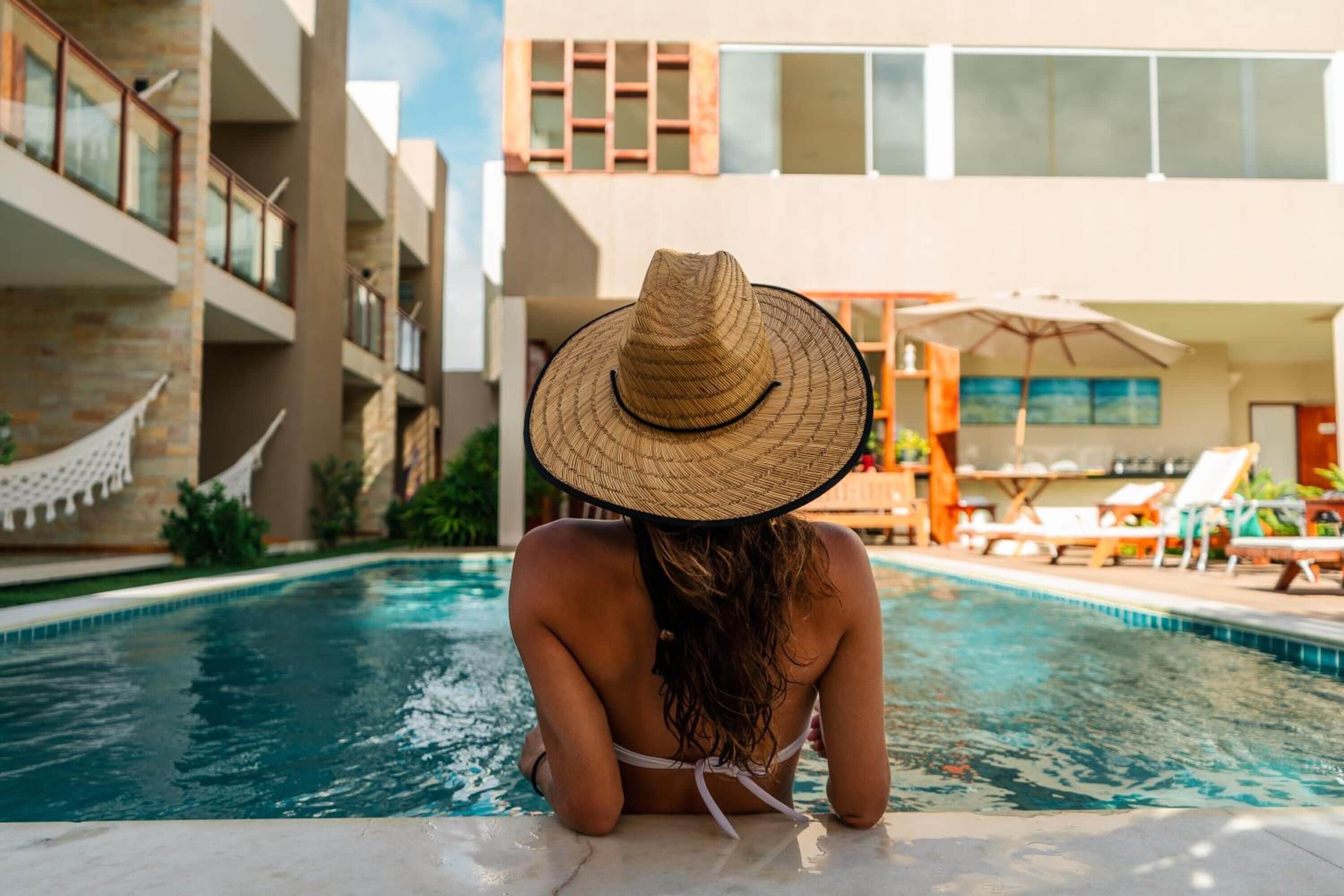 A person sitting by a pool with a view of a modern building with balconies and a hammock.