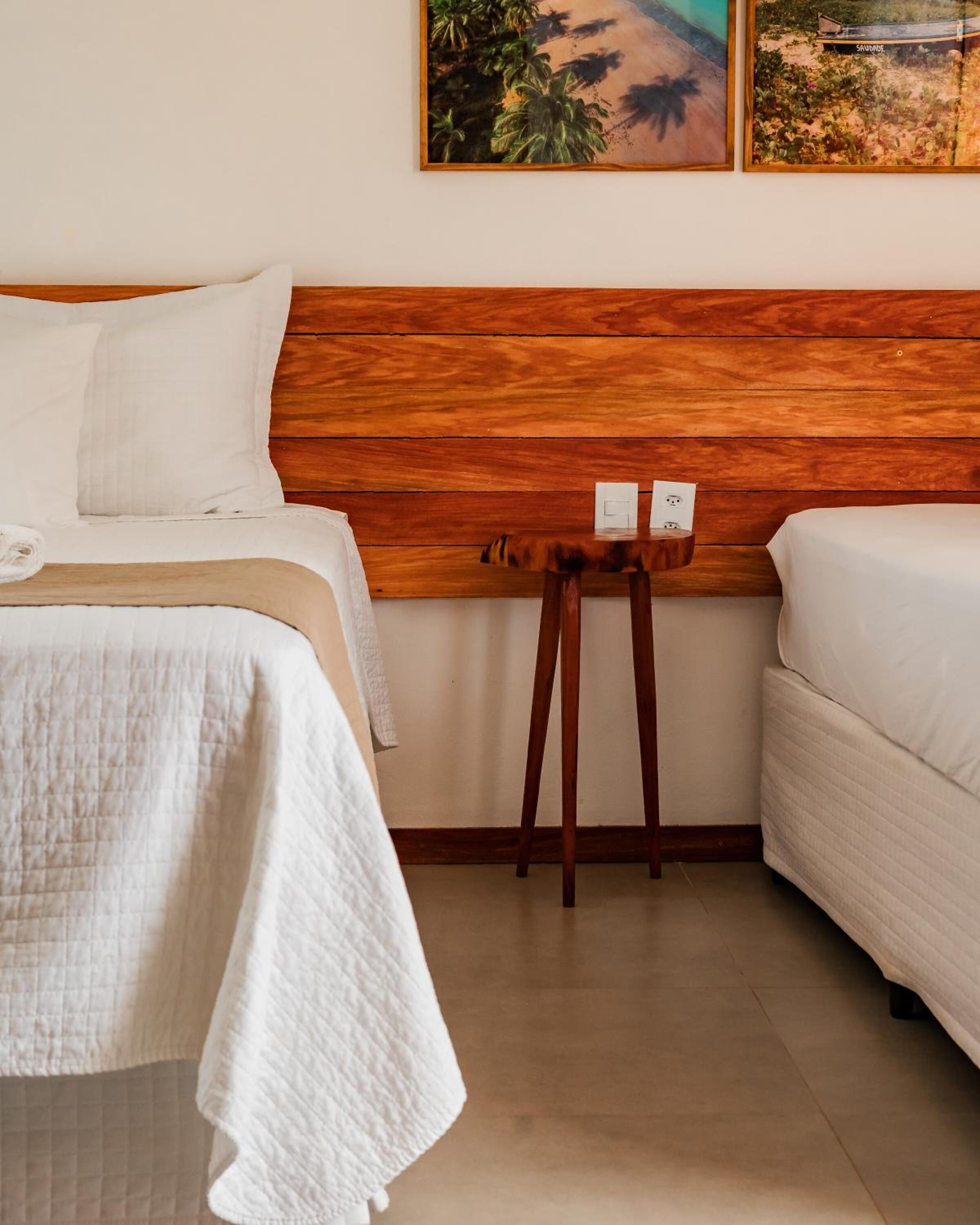 A hotel room with a wooden headboard, two beds, a small wooden table, and a painting on the wall.