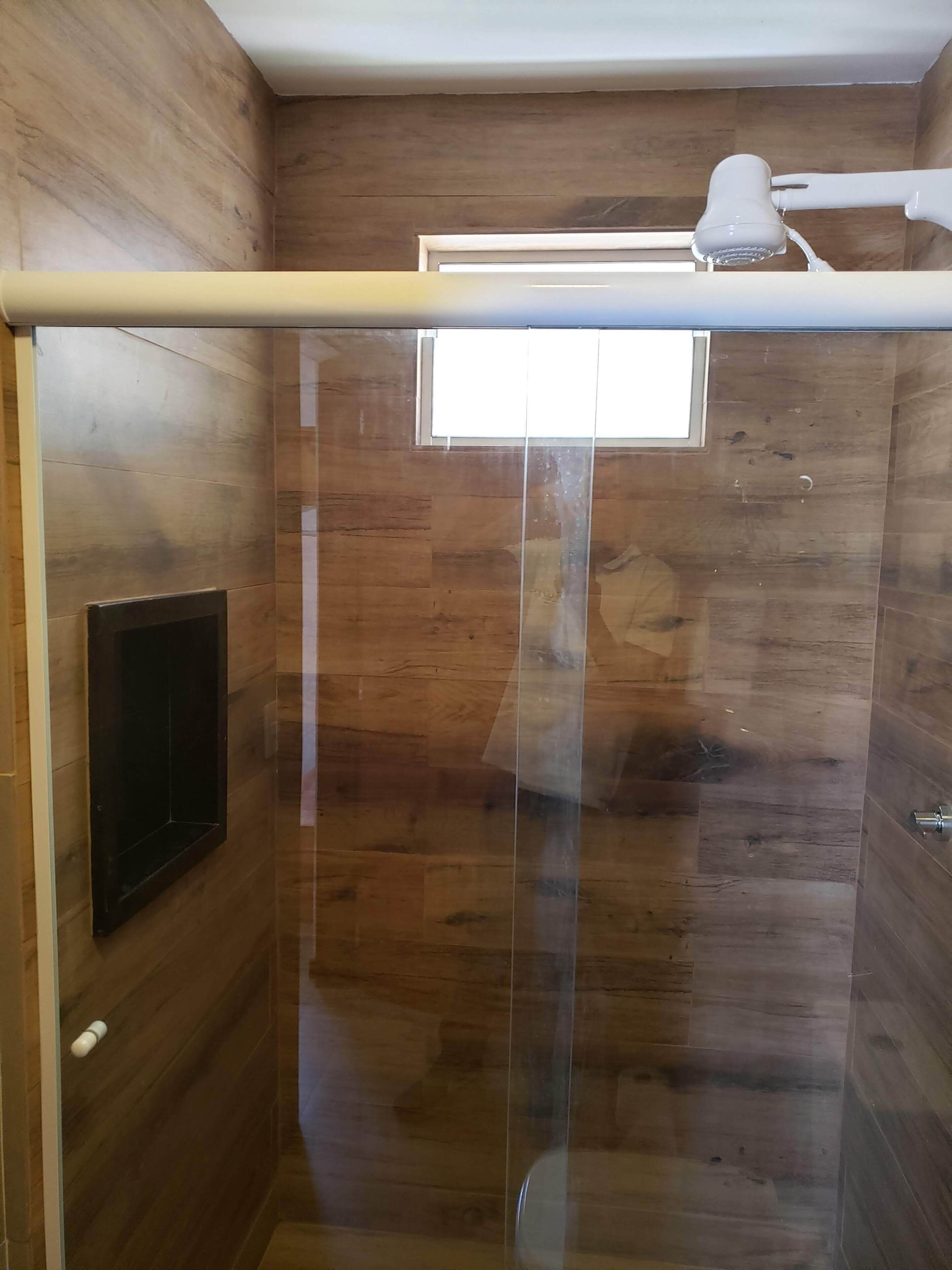 A shower with a glass door, wooden panel walls, and a mounted TV.