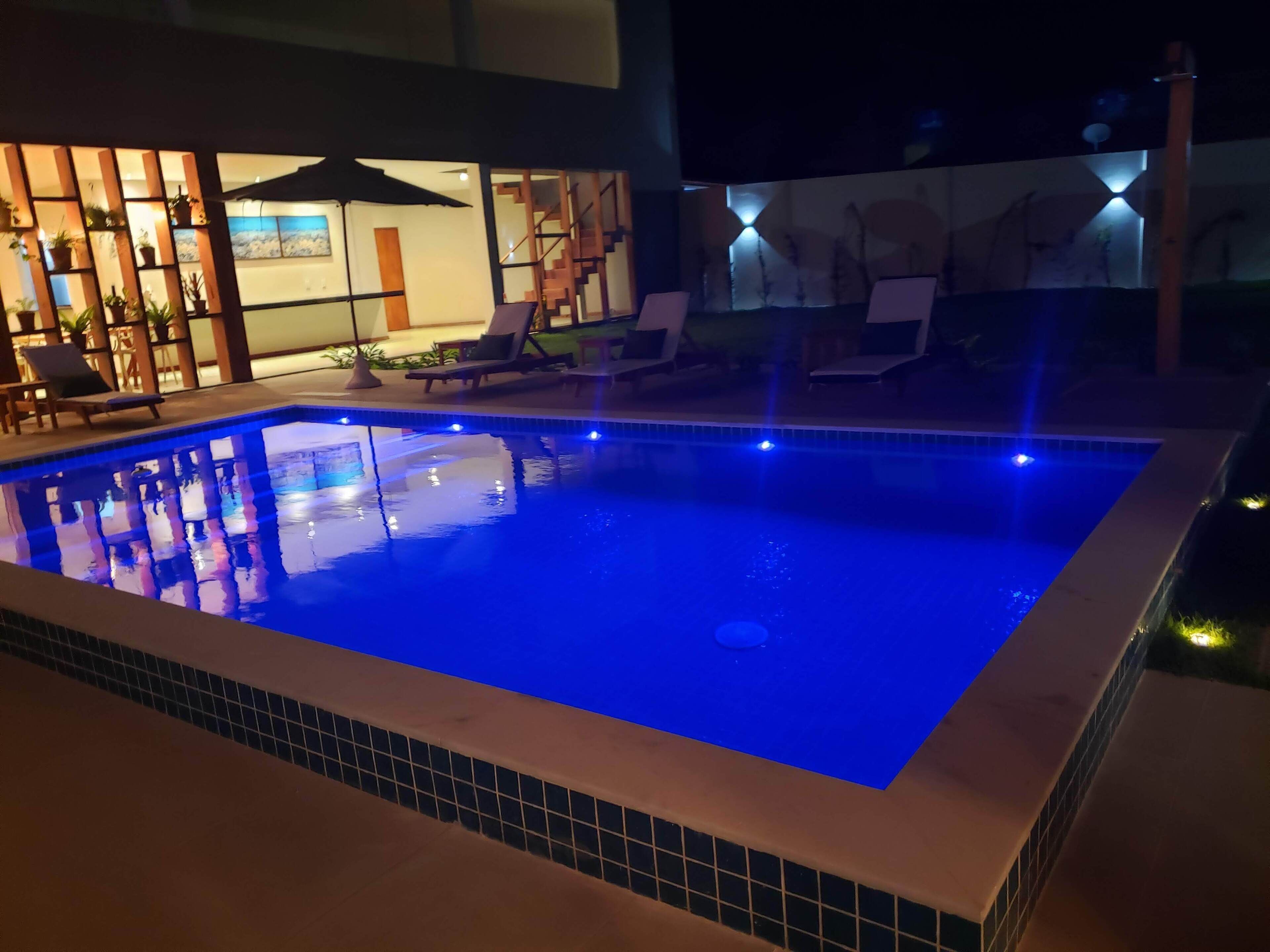 Zwembad met blauwe LED-verlichting, omringd door ligbedden en een overdekt zitgedeelte met planten.
