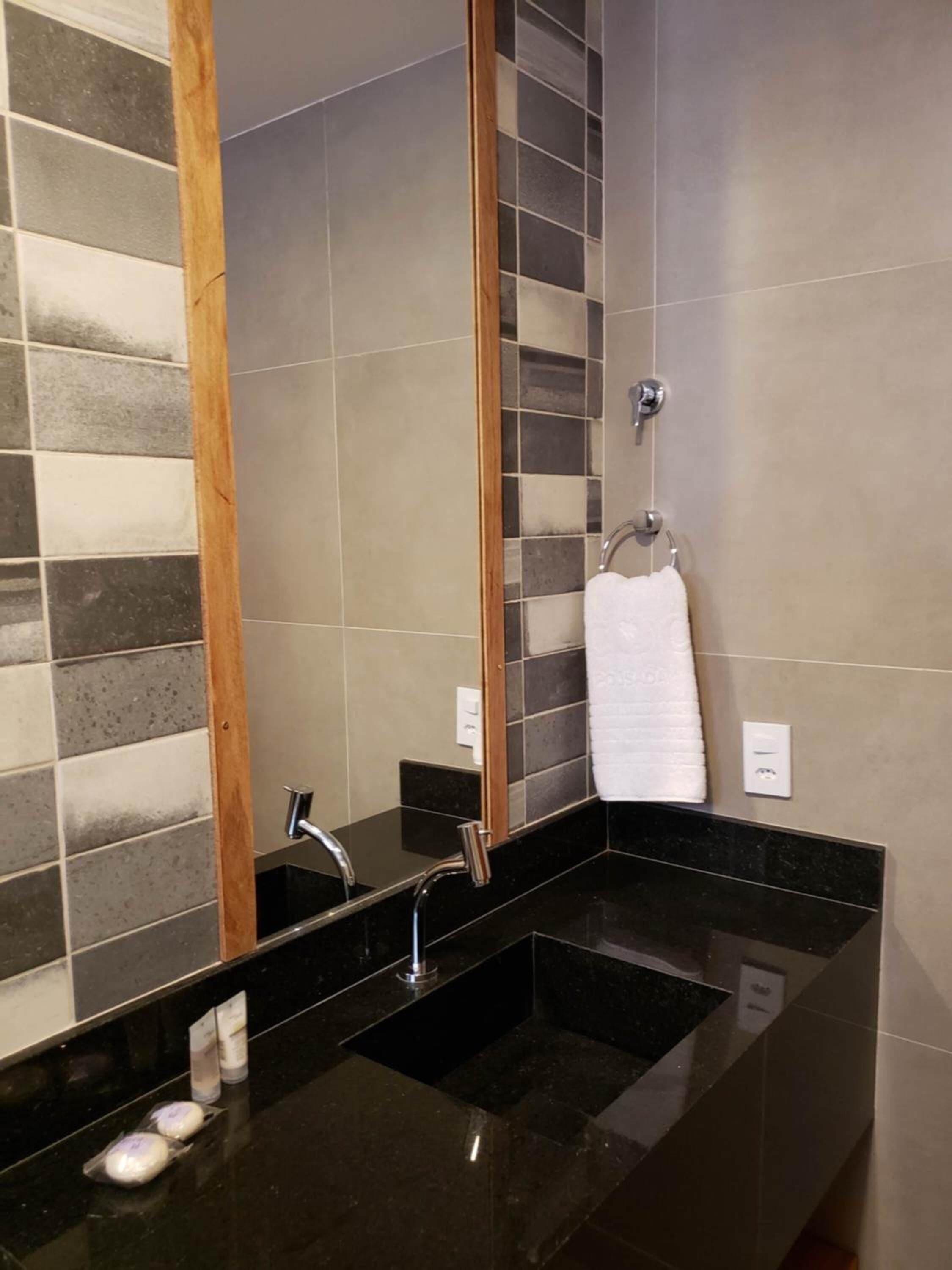 A modern bathroom with a black countertop, a mirror, and a towel rack.