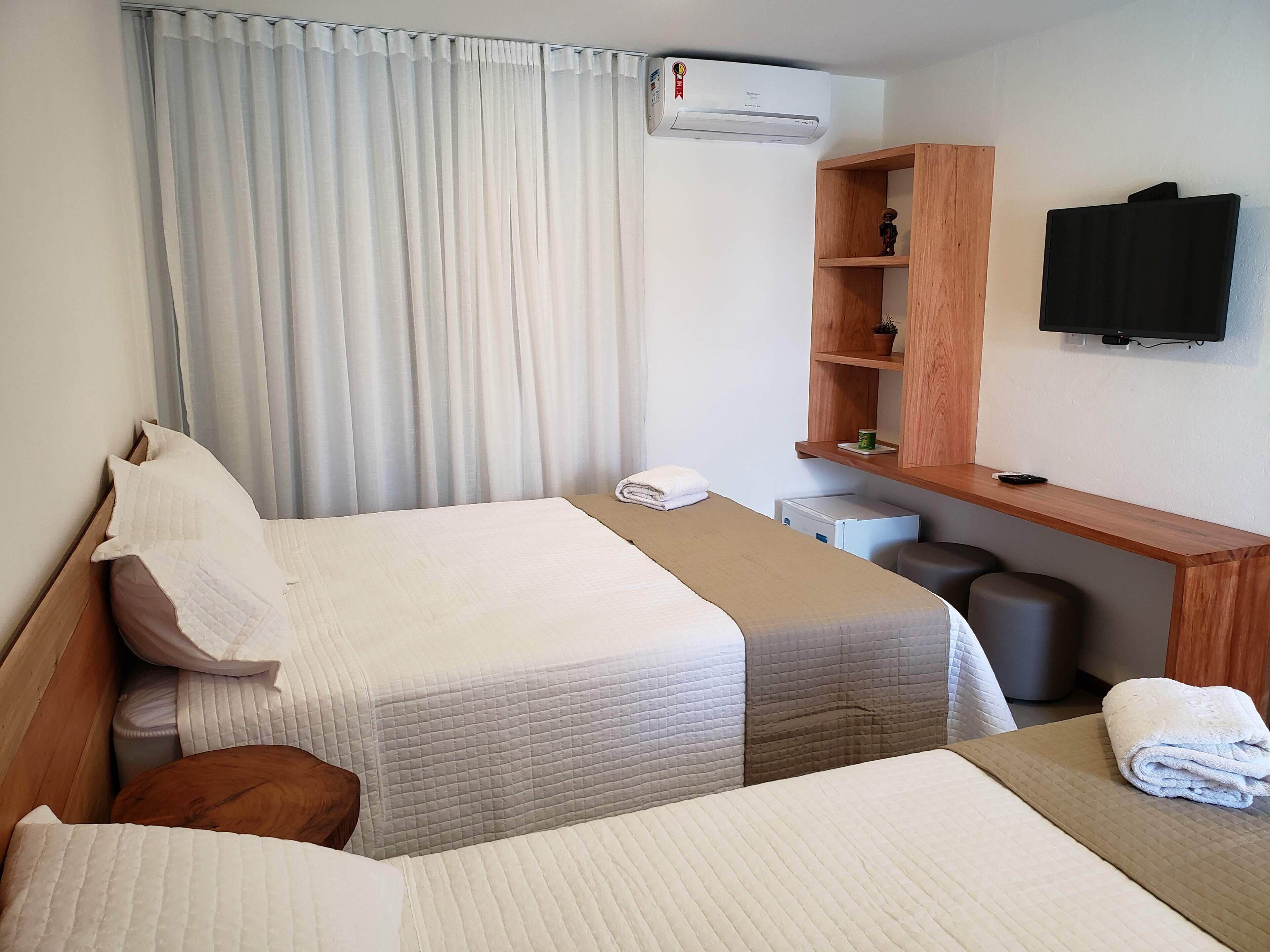 A hotel room with two beds, a desk, a television, and an air conditioning unit.